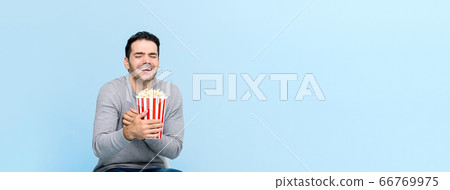 Young man holding popcorn laughing while watching movie 66769975