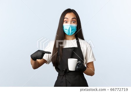 Covid-19, social distancing, small coffee shop business and preventing virus concept. Excited asian barista, female cafe employee in medical mask and gloves pointing at mug with coffee 66772719