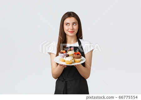 Grocery store employees, small business and coffee shops concept. Friendly smiling waitress bring desserts to cafe vistitor. Smiling cute barista showing delicious cupcakes on menu 66775554