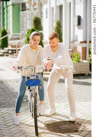 Woman learning riding a bike and a man helping her Woman learning riding a bike and a man helping her 66776441