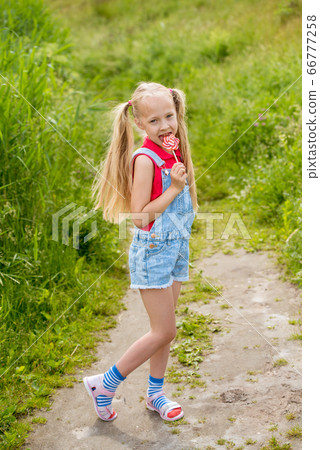 Blonde little girl with long hair and candy on a stick Blonde little girl with long hair and candy on a stick 66777258