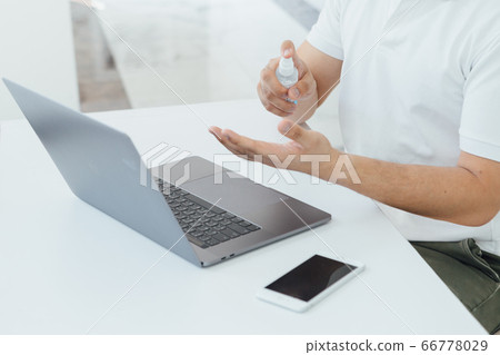 A man using the spray while working at home with his mask on A man using the spray while working at home with his mask on 66778029