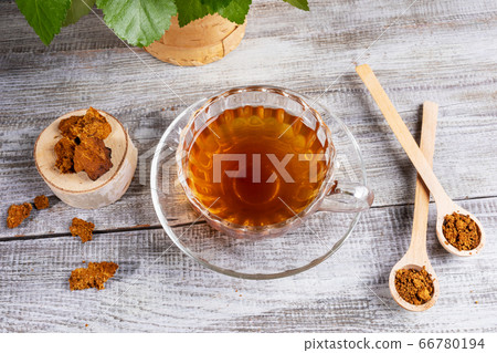 Healing infusion of birch mushroom chaga in figured glass cup and chaga pieces on wooden table. Trendy superfood drink. Healthy for immunity chaga mushroom coffee or tea. Alternative herbal medicine. Healing infusion of birch mushroom chaga in figured glass cup and chaga pieces on wooden table. Trendy superfood drink. Healthy for immunity chaga mushroom coffee or tea. Alternative herbal medicine. 66780194