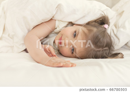 Little girl 3 years old lies on bed on under white 66780303