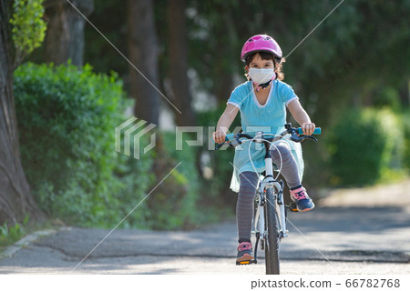 Little girl in protective medical mask rides a bike Little girl in protective medical mask rides a bike 66782768