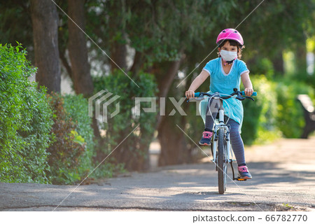 Little girl in protective medical mask rides a bike 66782770