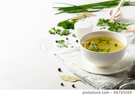 Chicken broth with green onion in white bowl on white table. Copy space. Chicken broth with green onion in white bowl on white table. Copy space. 66785089