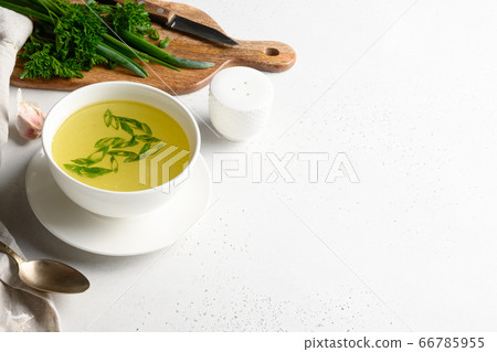 Chicken broth with green onion in white bowl on white table. Copy space. Chicken broth with green onion in white bowl on white table. Copy space. 66785955