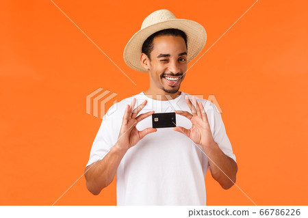 Relaxed and cheeky cute african-american man in white t-shirt, summer hat, wink camera assured and pleased, recommend bank service, holding credit card, standing orange background Relaxed and cheeky cute african-american man in white t-shirt, summer hat, wink camera assured and pleased, recommend bank service, holding credit card, standing orange background 66786226
