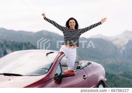 Happy woman sits in a red convertible car with a beautiful view Happy woman sits in a red convertible car with a beautiful view 66786227