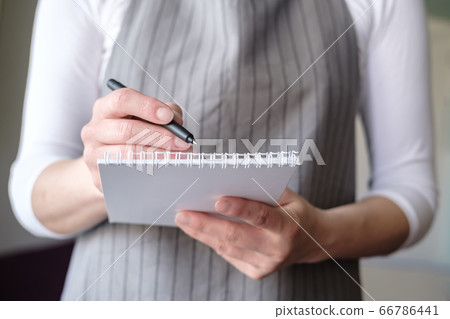 Waitress in a cafe in an apron with a notebook and pen takes an order from the client and writes it Waitress in a cafe in an apron with a notebook and pen takes an order from the client and writes it 66786441