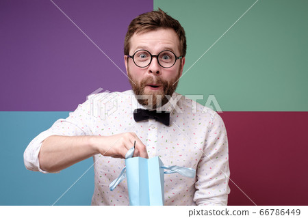 Attractive man is surprised by an unexpected surprise, he takes a gift from a package with a 66786449