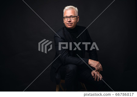 Serious businessman wearing glasses with white hair at the camera with a focused expression against a black studio background 66786817