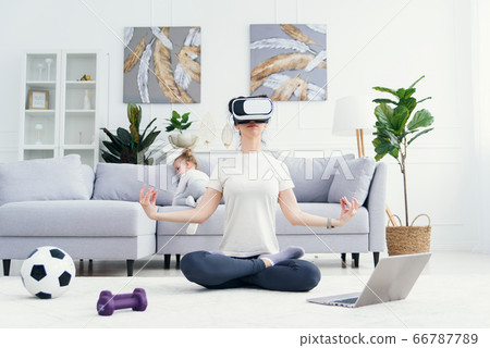 Young mom spending time with her little kids, meditating in lotus yoga position while her children playing at home on background. 66787789