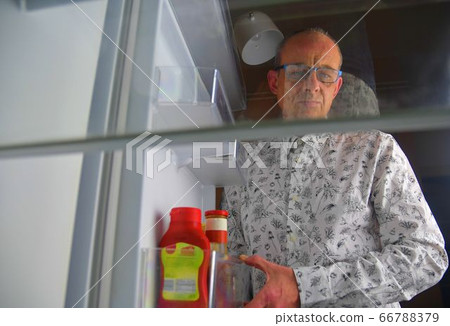 Portrait of a hungry man looking for food in refrigerator. Eating and diet concept - confused middle-aged man looking for food in empty fridge at kitchen Portrait of a hungry man looking for food in refrigerator. Eating and diet concept - confused middle-aged man looking for food in empty fridge at kitchen 66788379