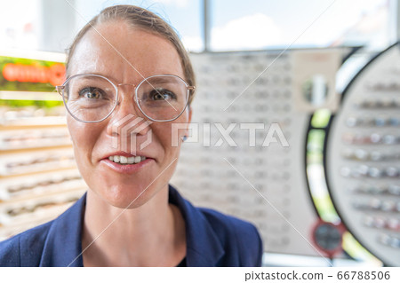 A young attractive woman in an optics store tries on new glasses. copy space A young attractive woman in an optics store tries on new glasses. copy space 66788506