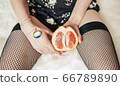 Girl in fishnet stockings with LGBT medallion holds a sexy grapefruit in her hand 66789890