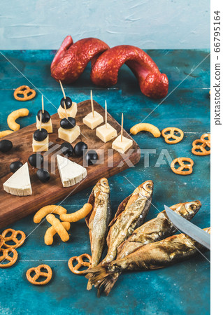 Sausage slices with cheese cubes, olives and crackers on a wooden board with dry fish 66795164