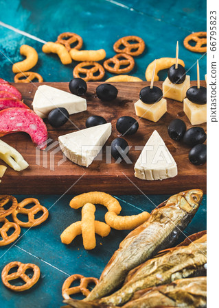 Snack board with sausage slices, cheese cubes and black olives with crackers and dry fish Snack board with sausage slices, cheese cubes and black olives with crackers and dry fish 66795823