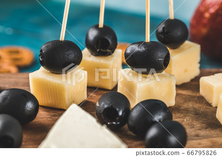 Cheese cubes and black olives on a wooden board with crackers on the blue table Cheese cubes and black olives on a wooden board with crackers on the blue table 66795826