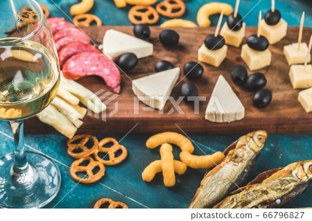 Pepperoni slices, cheese and black olives on a wooden board with crackers and a glass of white wine Pepperoni slices, cheese and black olives on a wooden board with crackers and a glass of white wine 66796827