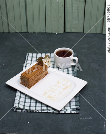 A slice of cake with caramel sauce and a cup of tea on a checked towel A slice of cake with caramel sauce and a cup of tea on a checked towel 66796908