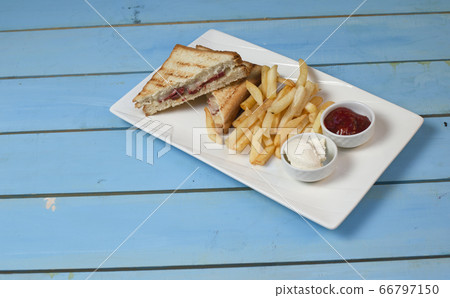 Club sandwiches served with fried potatoes in white plate with ketchup and mayonnaise on blue table 66797150