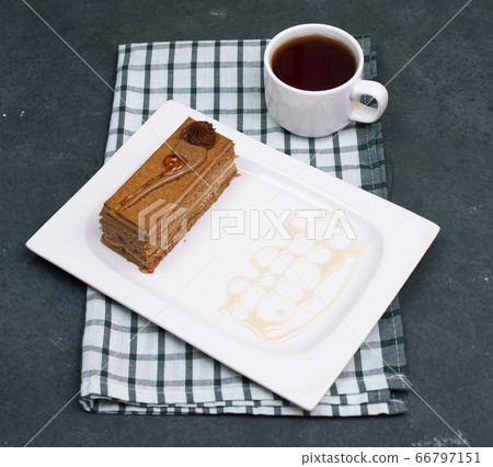 A slice of cake with caramel sauce and a cup of tea on a checked towel, top view A slice of cake with caramel sauce and a cup of tea on a checked towel, top view 66797151