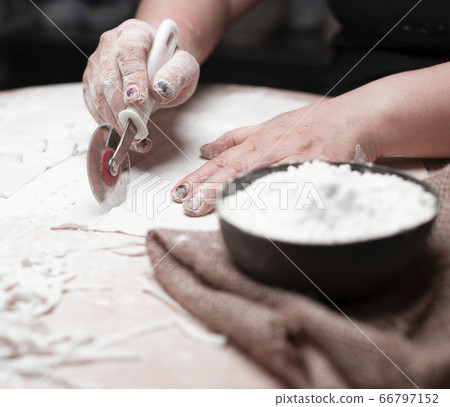 A cook cutting ravioli dough, flour in a black bowl A cook cutting ravioli dough, flour in a black bowl 66797152