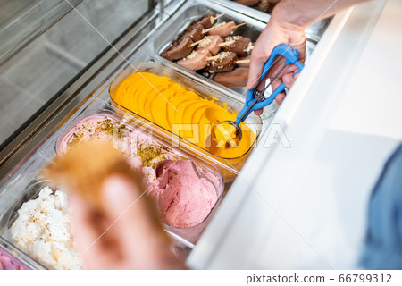Salesman picking ice cream with a spoon from refrigerator in the shop 66799312
