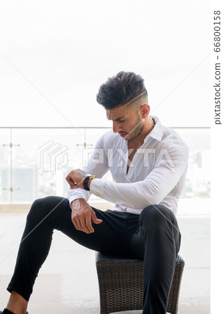 Young handsome bearded Persian businessman checking the time against view the city 66800158