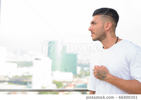Profile view of young handsome bearded Persian man looking at view of the city Profile view of young handsome bearded Persian man looking at view of the city 66800301