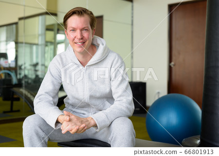 Happy young handsome man with hoodie smiling and sitting at the gym Happy young handsome man with hoodie smiling and sitting at the gym 66801913