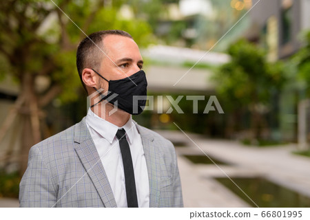 Face of Hispanic bald businessman thinking and wearing mask in the city with nature Face of Hispanic bald businessman thinking and wearing mask in the city with nature 66801995