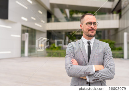 Handsome Hispanic bald bearded businessman thinking with arms crossed in the city Handsome Hispanic bald bearded businessman thinking with arms crossed in the city 66802079