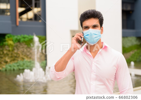 Young Indian businessman with mask talking on the phone in the city outdoors 66802306