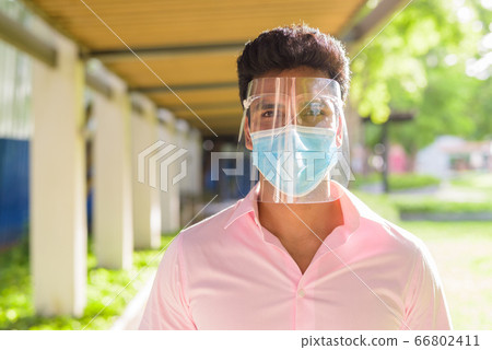 Face of young Indian businessman with mask and face shield at the park outdoors 66802411
