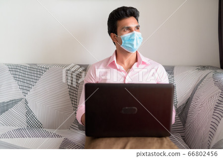 Young Indian businessman with mask thinking while using laptop and staying at home under quarantine Young Indian businessman with mask thinking while using laptop and staying at home under quarantine 66802456