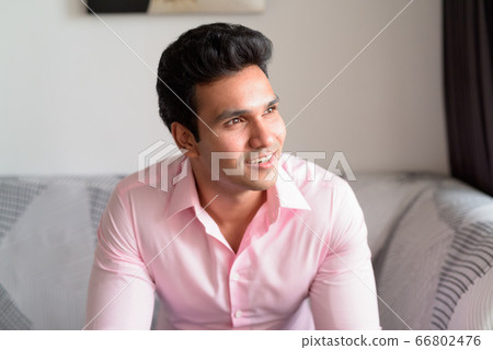 Face of happy young Indian businessman thinking and looking out the window at home Face of happy young Indian businessman thinking and looking out the window at home 66802476