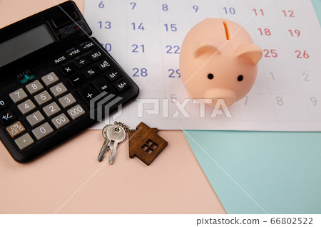 Day of buying or selling a house or payment for rent or loan. Piggy bank, wooden house keyring and calculator on white clean calendar 66802522