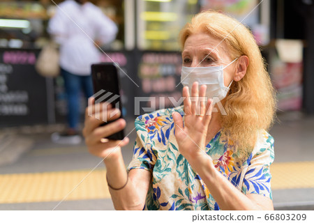 Blonde senior woman with mask video calling at the coffee shop outdoors Blonde senior woman with mask video calling at the coffee shop outdoors 66803209