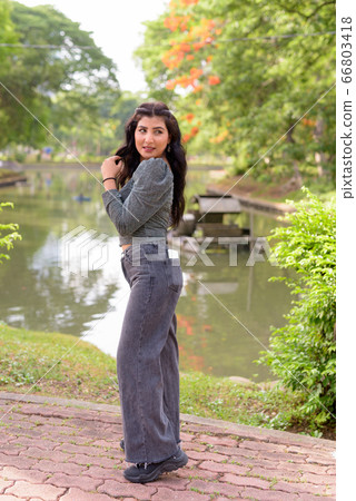 Full body shot of happy young beautiful Indian woman looking back at the park outdoors 66803418