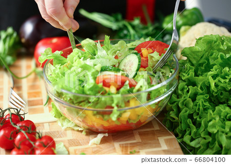 Young man mixing fresh salad with forks Young man mixing fresh salad with forks 66804100