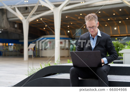 Mature businessman with eyeglasses using laptop in the city streets outdoors 66804986