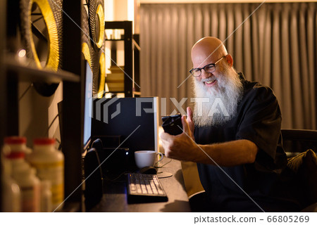 Happy mature bald bearded man video calling while working overtime at home late at night 66805269