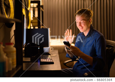 Happy young handsome businessman video calling while working from home at night Happy young handsome businessman video calling while working from home at night 66805364