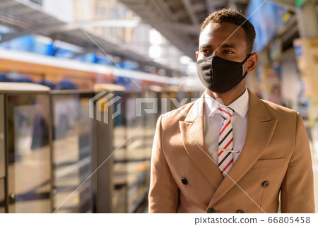 Young African businessman with mask thinking and waiting at the sky train station 66805458
