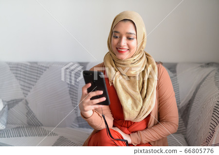 Happy young beautiful Muslim woman using phone in the living room at home 66805776