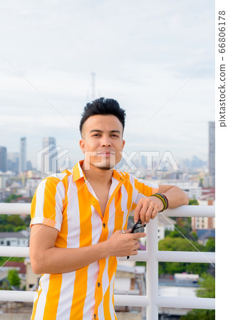 Young handsome multi ethnic man holding sunglasses against view of the city 66806178