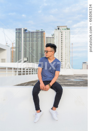 Full body shot of young handsome multi ethnic man with sunglasses sitting against view of the city Full body shot of young handsome multi ethnic man with sunglasses sitting against view of the city 66806334